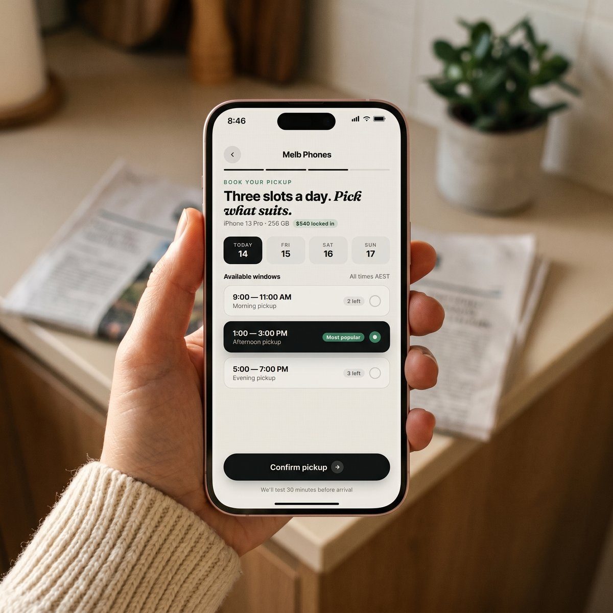 A hand holding an iPhone showing the PhoneFetch pickup booking screen